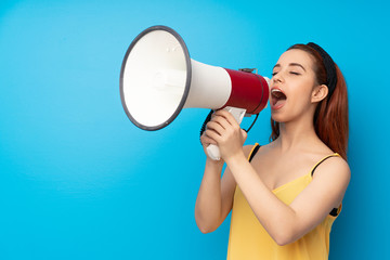 Young redhead woman over blue background shouting through a megaphone