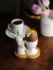 Easter dessert chocolate eggs filled with cream imitating white and yolk. Coffee cup. Served on holder with Easter bunny