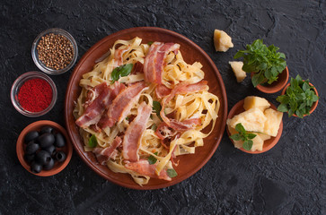 Classic pasta Carbonara, with bacon, egg, Parmesan cheese and Basil on a black slate background. Pieces of Parmesan, Basil, spices, olives are next to the table. the view from the top.