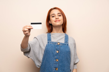 Fototapeta premium Young redhead woman over isolated background holding a credit card