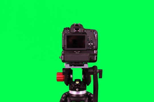 Dslr camera with empty screen on the tripod, isolated on green background. The chromakey. Green screen.