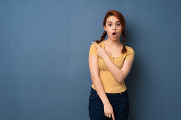 Young redhead woman over blue background surprised and pointing side