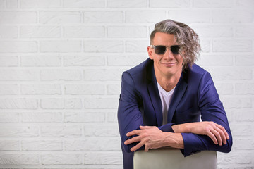 stylish businessman with curly long hair in sunglasses sitting on chair on white background