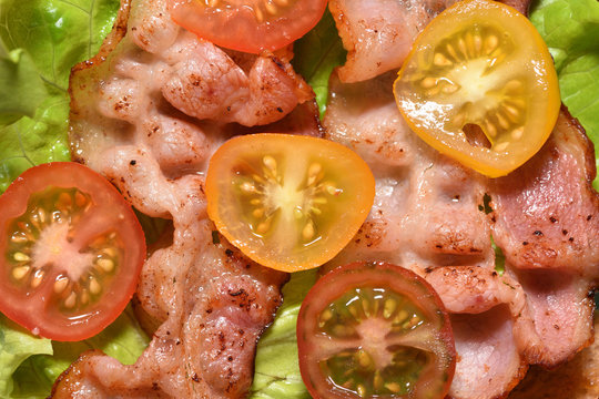 Fried bacon on lettuce and cherry tomatoes, for a tasty breakfast. Close-up