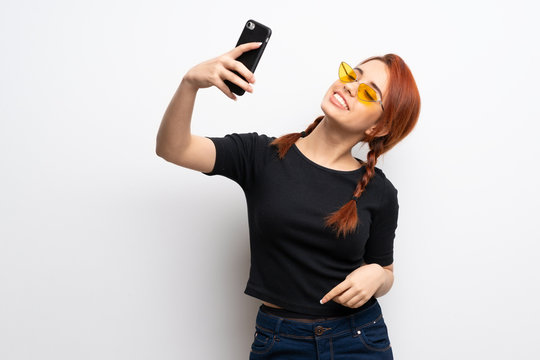 Young redhead woman over white wall making a selfie