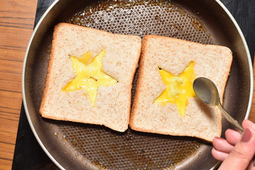 Roasting bread toasts with a star-shaped middle and a girl's hand fills it with a beaten egg to create a sandwich. Bread is fried for sandwiches in a pan with a non-stick coating, close-up