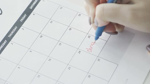 Woman's hand writing with red pen on calendar word Christmas