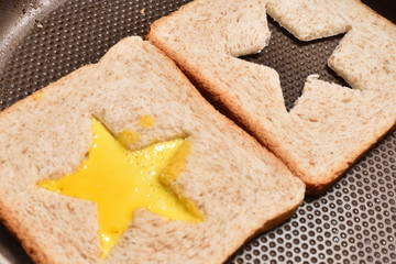 Roasting bread toasts with a star-shaped middle and omelette filled with egg to create a sandwich. Bread is fried for sandwiches in a pan with a non-stick coating, close-up