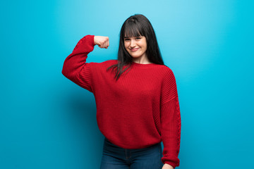 Woman with red sweater over blue wall Doing strong gesture