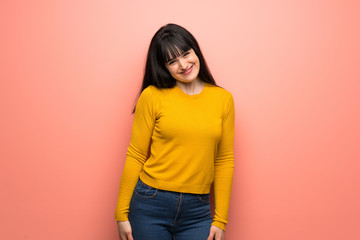 Woman with yellow sweater over pink wall smiling