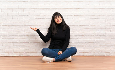 Woman sitting on the floor holding copyspace imaginary on the palm to insert an ad