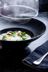 Cream soup is steaming in a black plate with on the black table. Photo for menu