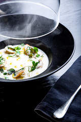 Cream soup is steaming in a black plate with on the black table. Photo for menu