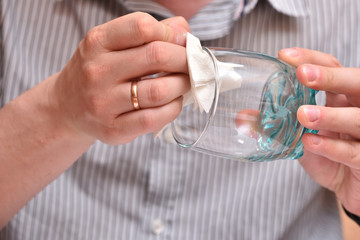 Man's hands, using a napkin, wipe a transparent glass for drinking so that there are no stains. Close-up