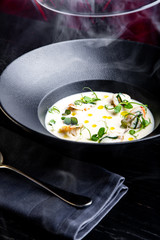 Cream soup is steaming in a black plate with on the black table. Photo for menu
