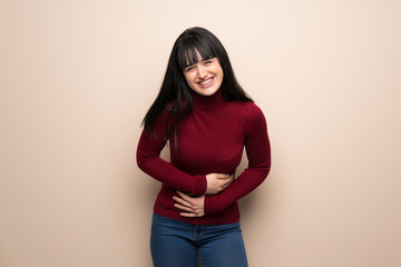 Young woman with red turtleneck smiling a lot while putting hands on chest