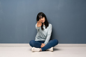 Woman sitting on the floor making stop gesture denying a situation that thinks wrong