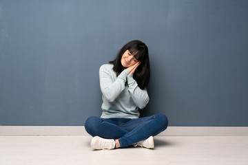 Woman sitting on the floor making sleep gesture in dorable expression
