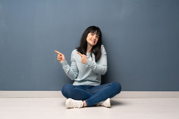 Woman sitting on the floor frightened and pointing to the side