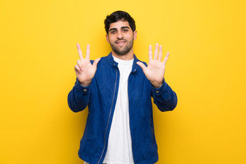 Man with blue jacket over yellow wall counting eight with fingers