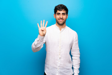 Young man over isolated blue wall happy and counting four with fingers