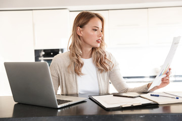 Blonde woman posing indoors at home using laptop computer work with documents.