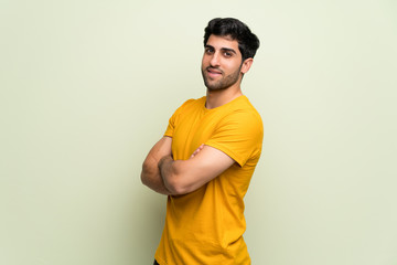 Young man over pink wall keeping the arms crossed in lateral position while smiling