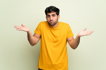 Young man over pink wall having doubts while raising hands and shoulders