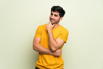 Young man over pink wall looking to the side with the hand on the chin