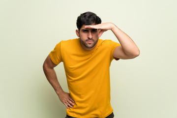 Young man over pink wall looking far away with hand to look something