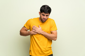 Young man over pink wall having a pain in the heart