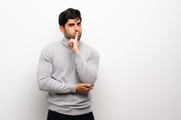 Young man over isolated white wall showing a sign of silence gesture putting finger in mouth