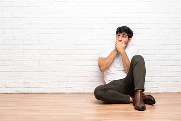 Young man sitting on the floor covering mouth and looking to the side