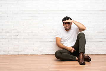 Young man sitting on the floor looking far away with hand to look something