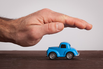 Small retro, blue car covering by male hand.  Protection, car insurance.