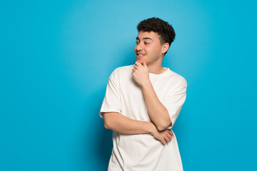 Fototapeta premium Young man over blue background looking to the side with the hand on the chin