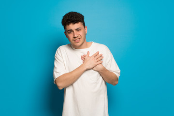 Young man over blue background having a pain in the heart