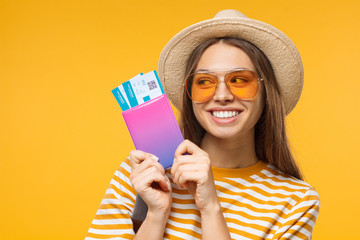 Smiling young dreaming girl tourist holding passport with flight tickets, isolated on yellow background