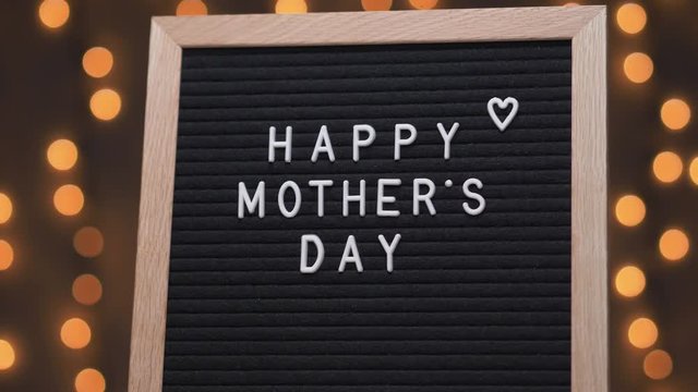 Black letter board with HAPPY MOTHER'S DAY title on it. Camera rotating around the sign showing the beautiful bokeh balls in the background.