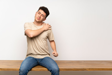 Young man sitting on table suffering from pain in shoulder for having made an effort