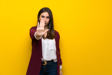 Young woman over yellow wall making stop gesture denying a situation that thinks wrong