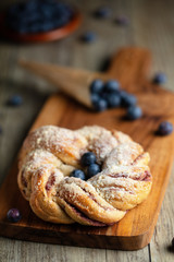 Blueberry pleated bun with powdered sugar and fresh berries on wooden board. Vertical composition.
