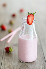 Healthy strawberry smoothie, milk shake, in single milk bottle with scattered berries and straw over a wood background. Vertical composition