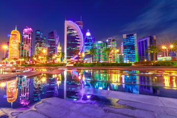 Fototapeta premium Capital of Qatar. Colorful Doha West Bay high rises illuminated at night reflections in downtown park. Scenic towers of Doha skyline, Middle East, Arabian Peninsula in Persian Gulf. Violet colors shot