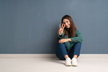 Young woman sitting on the floor happy and counting three with fingers