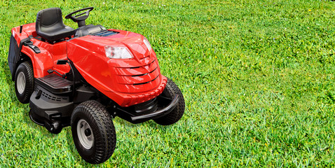 Gardening equipment advertisement template - red tractor mower on a green grass in the garden with copy space.