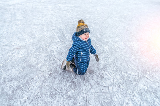 A small boy of 4-6 years old, kneeling, skating, in the winter in the city on an ice rink. Happy smiling, trying to ride the first steps on the rink. Free space for text.
