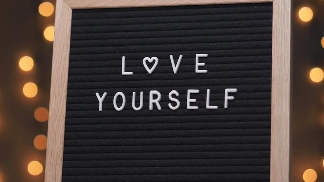 Black letter board with LOVE YOURSELF title on it. Camera rotating around the sign showing the beautiful bokeh balls in the background.