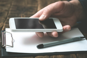 Mobile phone with blank screen in a businessman hands on an office table background. Contact us.