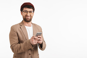 Photo of caucasian man 30s wearing hipster hat smiling while holding and using smartphone
